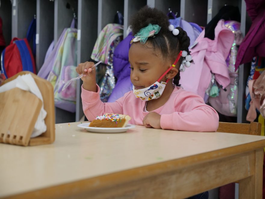 A preschool student eats a piece of pumpkin pie.