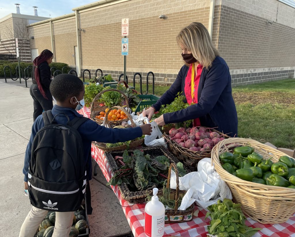 A student is handed a bag to collect fresh fruits and vegetables at Edison's produce stand.
