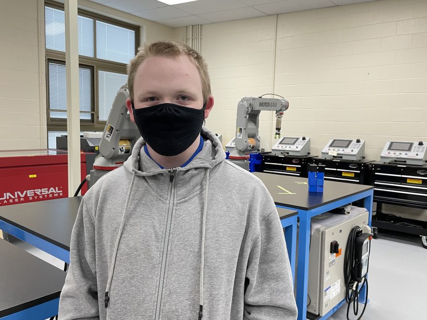 Riley McComas, a 10th grade student at Meadowdale, stands next to a piece of equipment in the Advanced Manufacturing classroom.