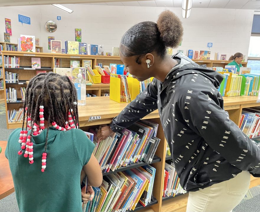 A Meadowdale student points to a book as she helps a Valerie student in the library.